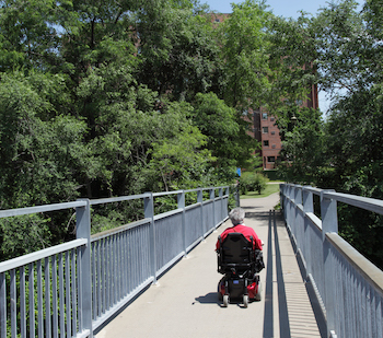 Safe Routes for Non-Drivers A senior woman in a power wheelchair, crossing a pedestrian bridge - Photo courtesy RTC